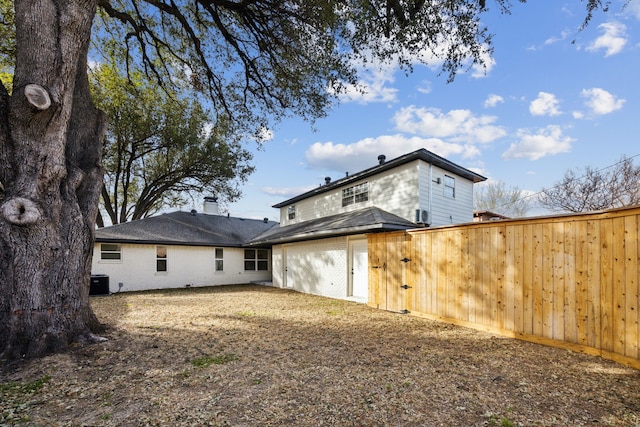 back of property with brick siding, an attached garage, fence, and central air condition unit