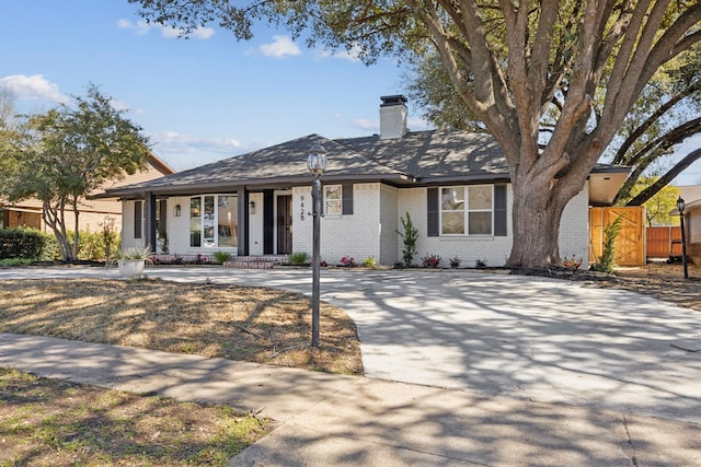 ranch-style home featuring a chimney, fence, and brick siding