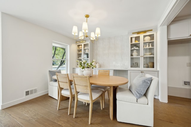 dining area featuring visible vents, a notable chandelier, baseboards, and wood finished floors