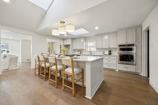 kitchen with wood finished floors, light countertops, double oven, a kitchen bar, and a sink