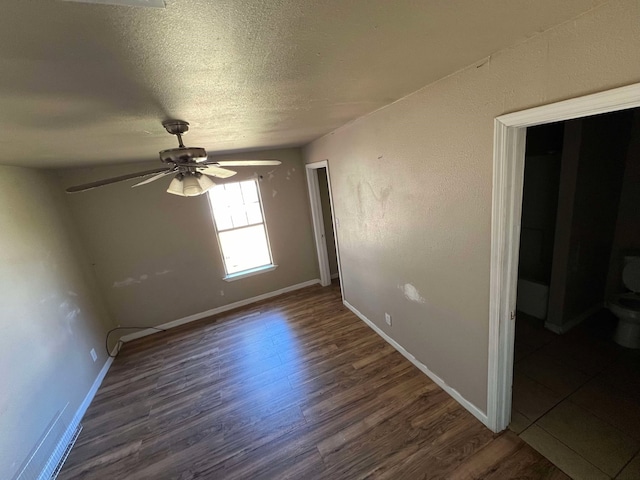 empty room featuring a textured ceiling, wood finished floors, a ceiling fan, and baseboards