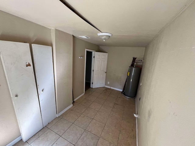 basement with water heater, light tile patterned floors, visible vents, and baseboards