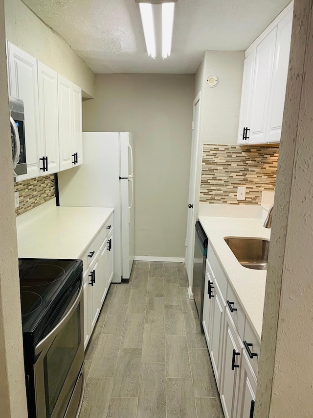 kitchen with a sink, stainless steel appliances, white cabinets, light countertops, and decorative backsplash