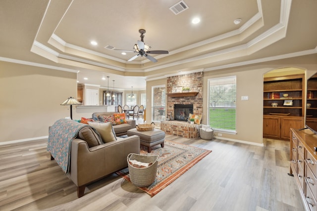 living room with a tray ceiling, light wood-style floors, and visible vents