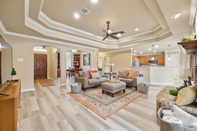 living room featuring light wood-type flooring, a tray ceiling, arched walkways, and visible vents