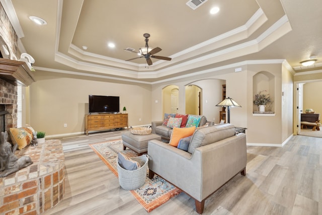 living room with a tray ceiling, a brick fireplace, visible vents, and arched walkways