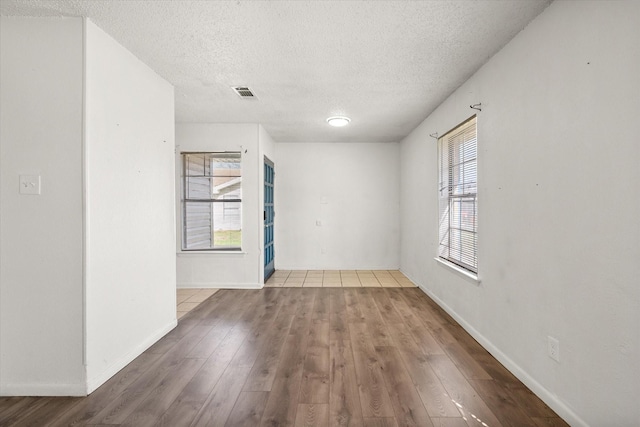 empty room featuring visible vents, a textured ceiling, baseboards, and wood finished floors