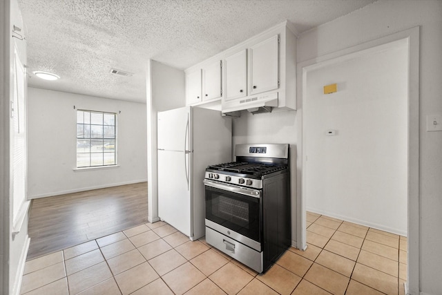 kitchen featuring stainless steel range with gas cooktop, light tile patterned floors, visible vents, white cabinets, and under cabinet range hood