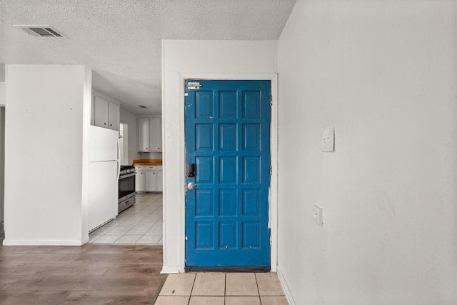 foyer entrance with light wood-style floors, visible vents, a textured ceiling, and baseboards