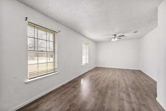 empty room with a textured ceiling, wood finished floors, a ceiling fan, and baseboards