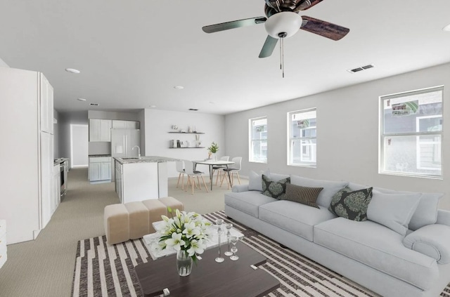 living room featuring ceiling fan, visible vents, and light colored carpet