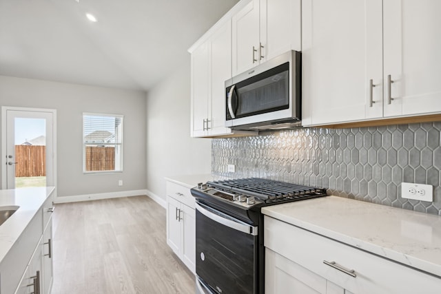 kitchen featuring lofted ceiling, light stone counters, backsplash, stainless steel microwave, and range with gas cooktop