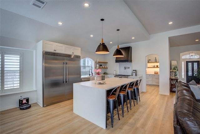 kitchen with open floor plan, light wood-style floors, premium range hood, stainless steel built in refrigerator, and visible vents