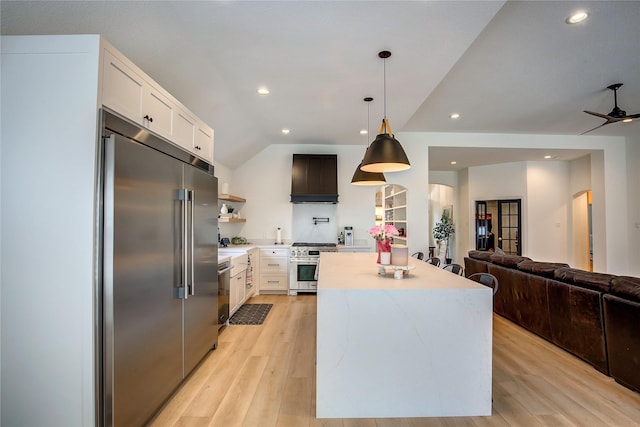 kitchen with light wood-style flooring, arched walkways, high end appliances, custom range hood, and light countertops