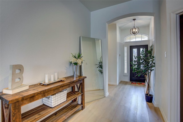 foyer entrance featuring a notable chandelier, light wood-style flooring, arched walkways, and baseboards