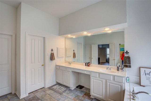 bathroom with double vanity, a sink, stone finish flooring, baseboards, and a tub