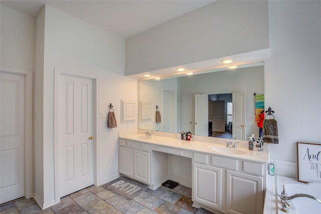 full bathroom featuring a tub to relax in, a sink, baseboards, double vanity, and stone finish floor