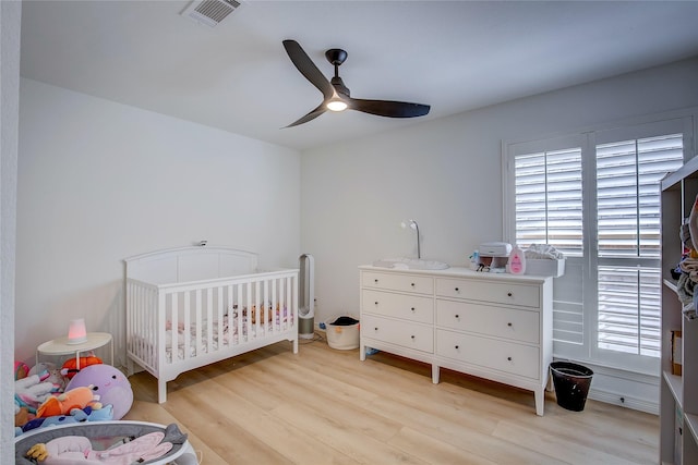 bedroom featuring ceiling fan, light wood finished floors, a crib, and visible vents