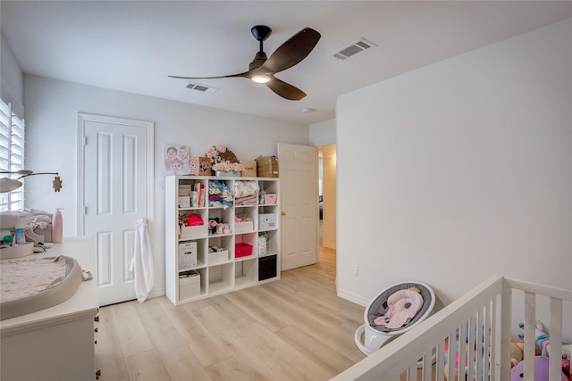 bedroom featuring ceiling fan, light wood finished floors, a nursery area, and visible vents