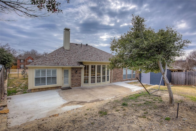 rear view of house featuring a patio, brick siding, a chimney, and fence