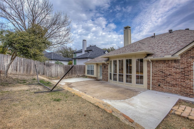 back of property featuring a patio, brick siding, a shingled roof, fence, and a chimney