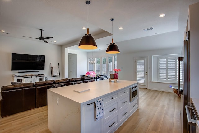 kitchen with stainless steel microwave, visible vents, light wood finished floors, and open floor plan