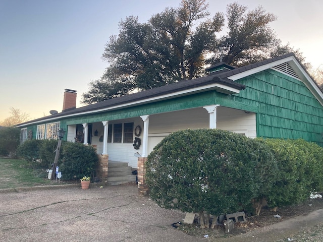 single story home featuring a porch, a chimney, and an attached garage