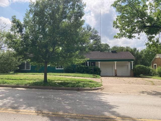 view of property hidden behind natural elements with an attached garage, concrete driveway, and a front lawn