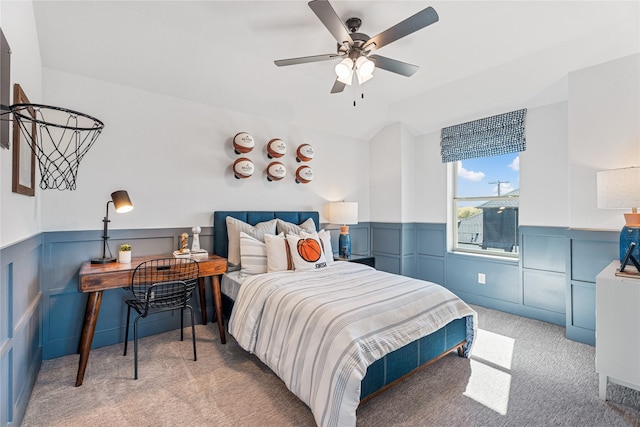 bedroom with a wainscoted wall, vaulted ceiling, a ceiling fan, and light colored carpet