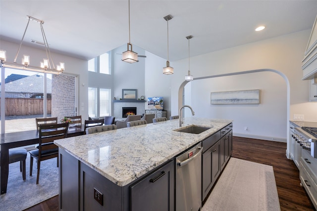 kitchen featuring light stone counters, stainless steel appliances, dark wood-type flooring, a sink, and a lit fireplace