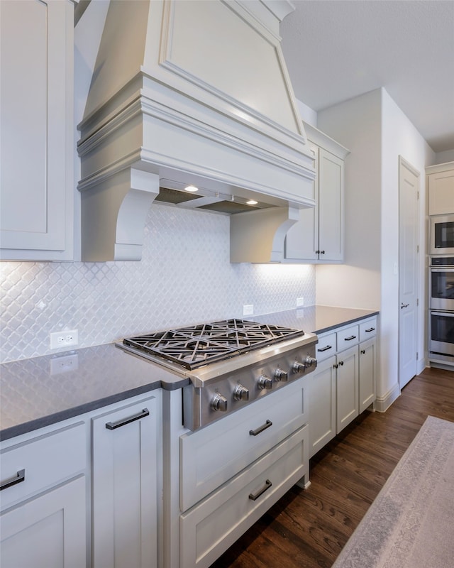 kitchen featuring tasteful backsplash, white cabinets, dark wood-type flooring, stainless steel appliances, and premium range hood