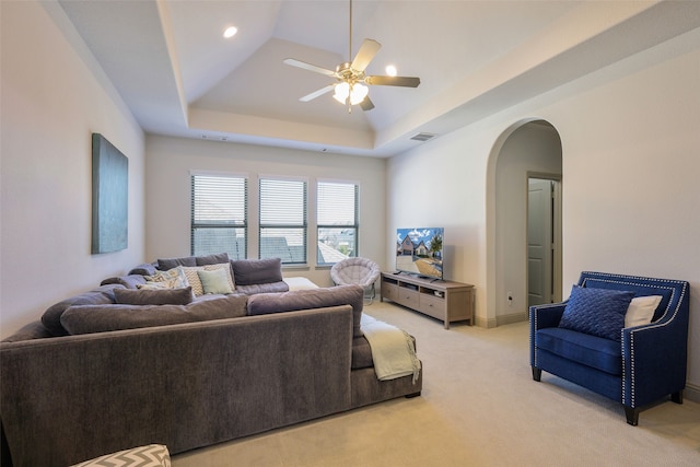 living room featuring arched walkways, a raised ceiling, visible vents, light carpet, and ceiling fan