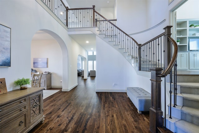 foyer entrance with arched walkways, stairway, a high ceiling, dark wood-type flooring, and baseboards