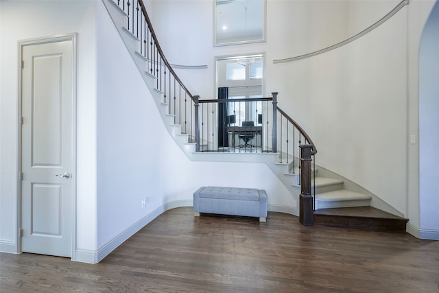 stairs with a towering ceiling, baseboards, and wood finished floors