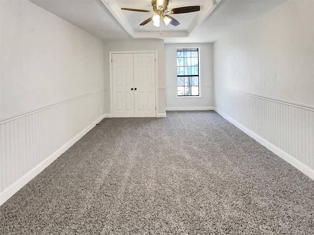 unfurnished bedroom with a tray ceiling, a closet, a wainscoted wall, and carpet flooring