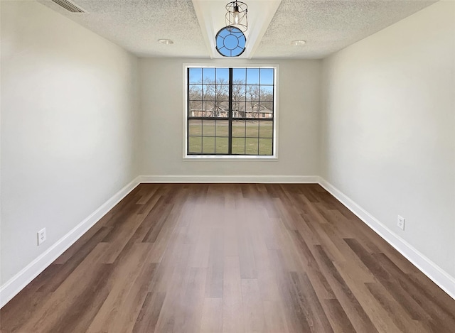 empty room with a textured ceiling, dark wood-type flooring, visible vents, and baseboards