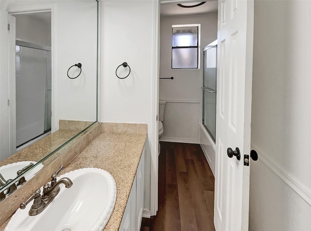 full bathroom featuring toilet, combined bath / shower with glass door, wood finished floors, and vanity