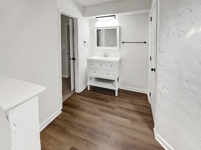 bathroom featuring a textured wall, vanity, baseboards, and wood finished floors