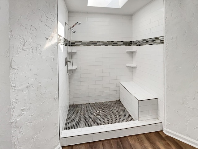 full bath featuring a skylight, a tile shower, wood finished floors, and a textured wall