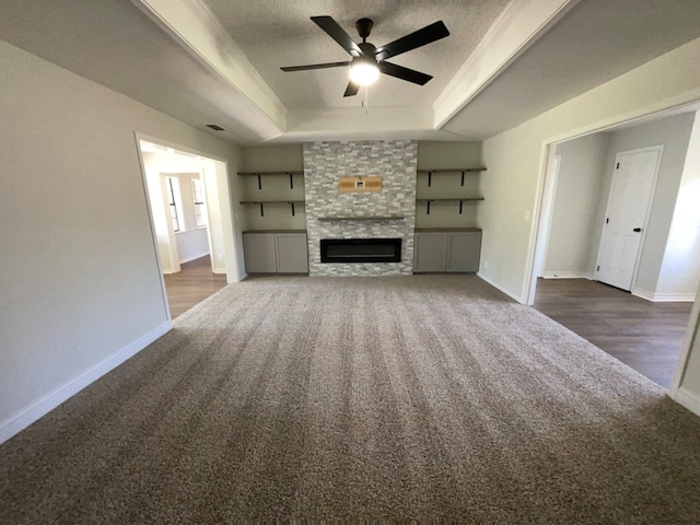 unfurnished living room featuring a large fireplace, carpet floors, a raised ceiling, and baseboards