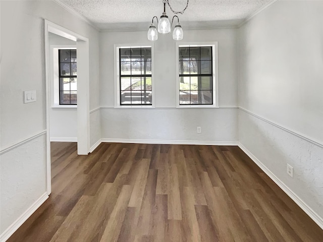 unfurnished dining area featuring ornamental molding, a textured ceiling, an inviting chandelier, and wood finished floors