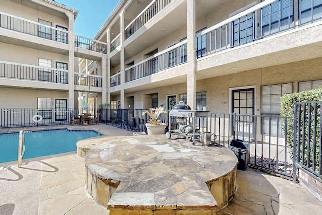 community pool with a patio, fence, and a grill