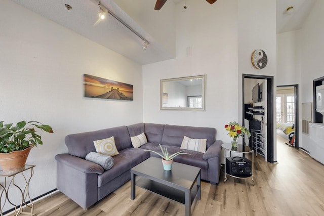 living area with track lighting, a towering ceiling, ceiling fan, and wood finished floors