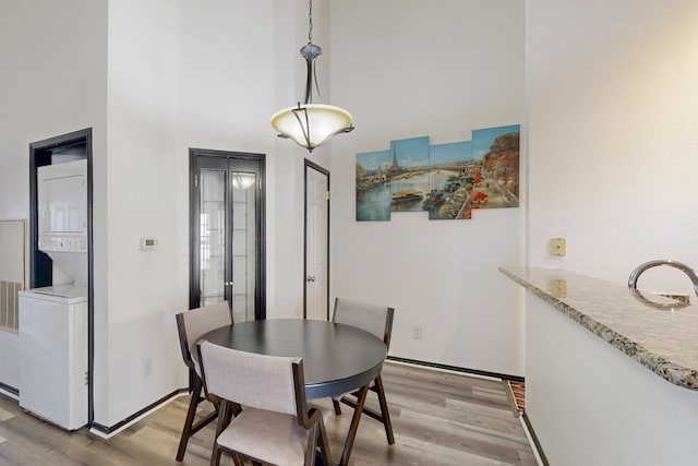 dining area with stacked washer / dryer, a towering ceiling, baseboards, and light wood finished floors