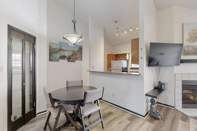 dining area with light wood finished floors, visible vents, a fireplace, and high vaulted ceiling