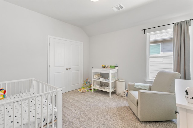 carpeted bedroom featuring a closet, visible vents, vaulted ceiling, and a crib