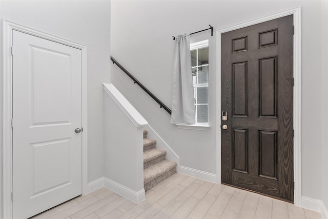 foyer with light wood-style flooring, stairway, and baseboards