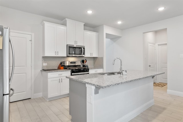 kitchen with appliances with stainless steel finishes, a sink, a kitchen island with sink, and white cabinetry