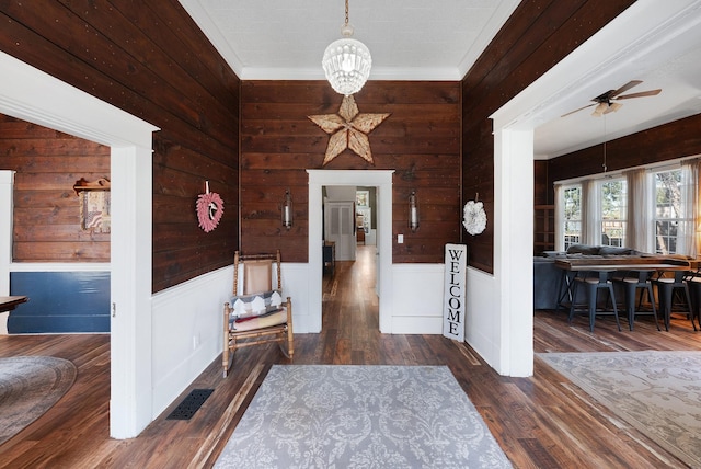 entryway with visible vents, crown molding, a wainscoted wall, ceiling fan with notable chandelier, and wood finished floors