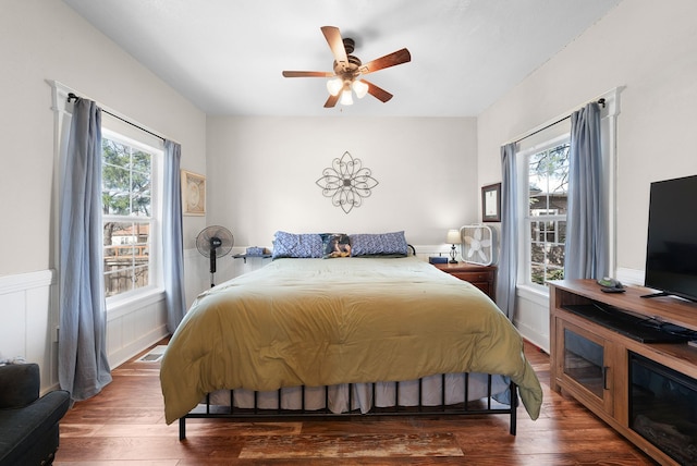 bedroom featuring hardwood / wood-style flooring, a ceiling fan, and a wainscoted wall